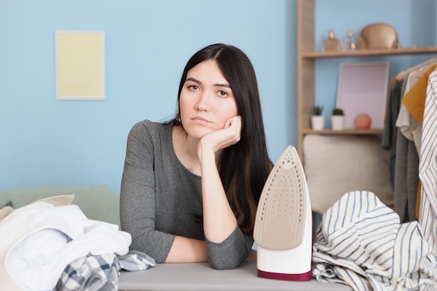 Triest huisvrouw strijken kleren in het interieur van de kamer