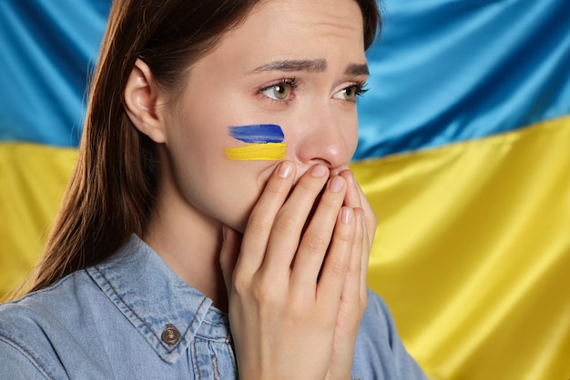 Triest jonge vrouw met gevouwen handen in de buurt van Oekraïense vlag close-up Ruimte voor tekst