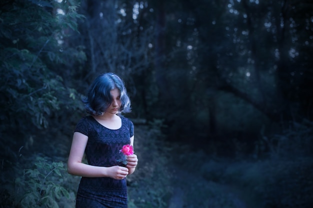 Triest meisje met blauw haar en roze roos in nacht bos