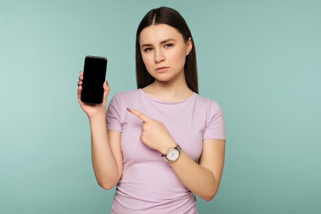 Triest meisje wijst naar smartphone op blauw