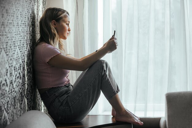 Triest mooi meisje dat thuis naar de telefoon kijkt