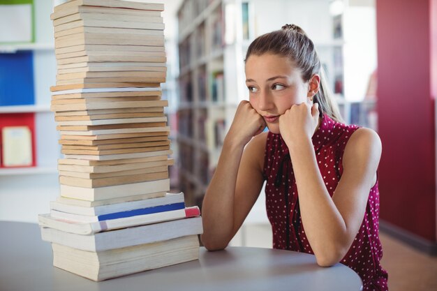 Triest schoolmeisje kijken naar stapel boeken in bibliotheek