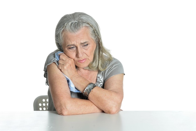 Triest senior vrouw aan tafel poseren geïsoleerd op witte achtergrond