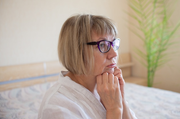 Triest senior vrouw met wit haar is verdrietig in haar huis in slaapkamer Eenzaamheid concept verdriet