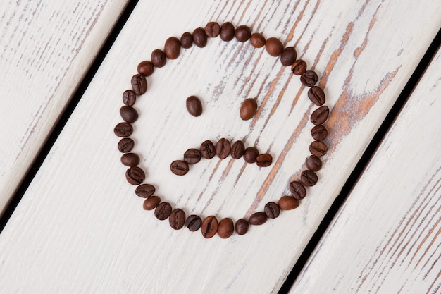 Triest smileygezicht gemaakt van koffiebonen. Bruin geroosterde granen op wit hout.