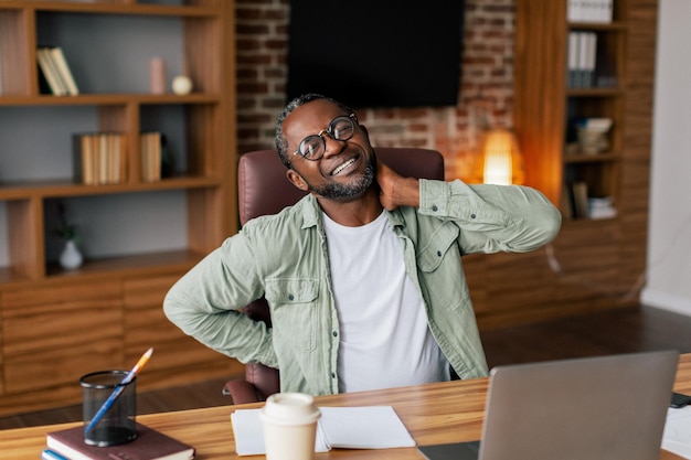 Triest volwassen Afro-Amerikaanse mannelijke manager in een bril casual lijdt aan rug- en nekpijn door stress