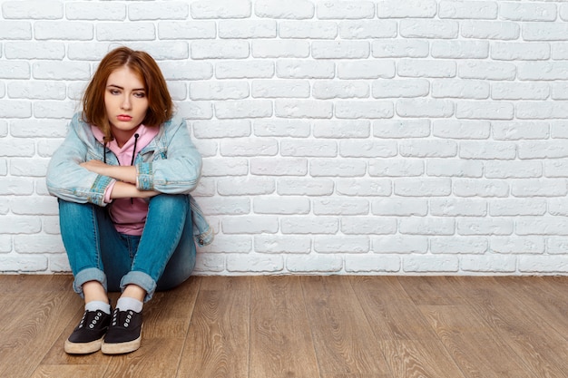 Triest vrouw zittend op de vloer in de buurt van muur