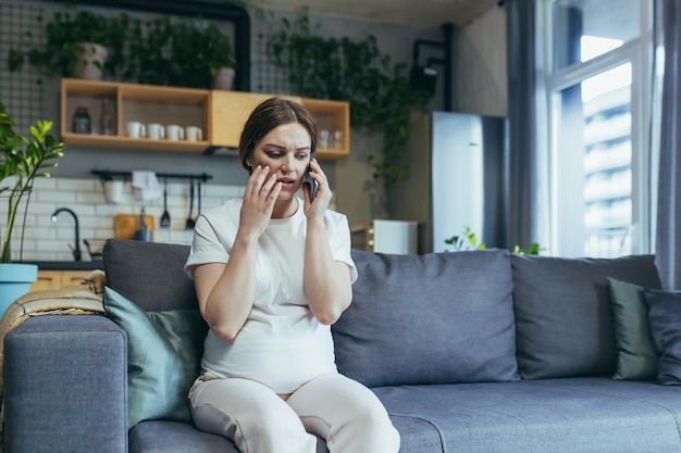 Triest zwangere vrouw thuis angstig praten aan de telefoon zittend op de bank