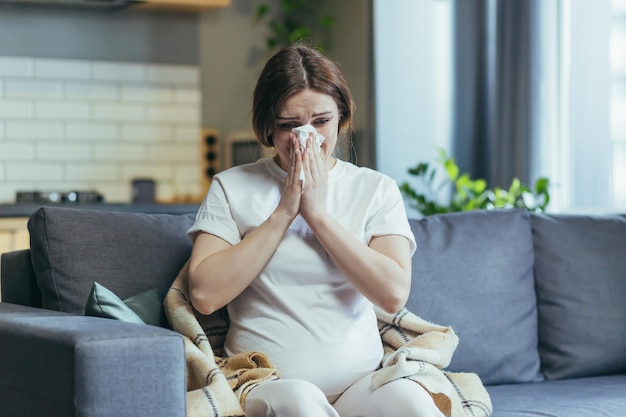 Triest zwangere vrouw thuis zittend op de bank en huilen heeft een loopneus en allergieën niest in een servet