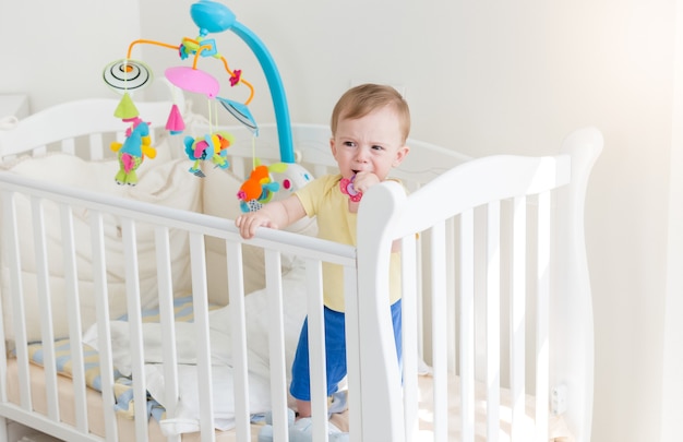 Trieste 10 maanden oude babyjongen die huilt en vasthoudt aan de zijkant van de wieg