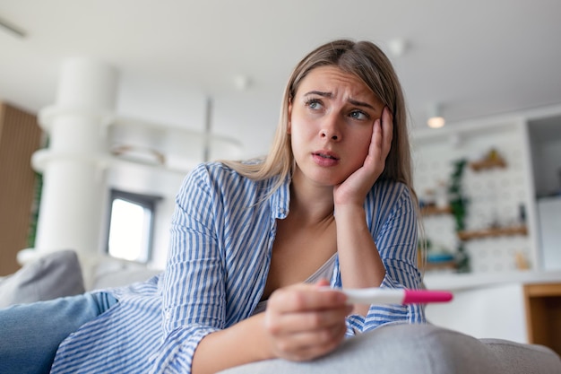 Trieste bezorgde vrouw die haar recente zwangerschapstest controleert terwijl ze thuis op de bank zit Zwangerschapsbevalling en familieproblemen concept ongewenste zwangerschap