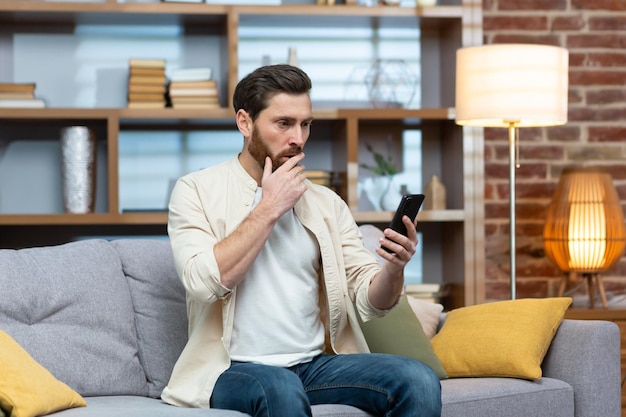 Trieste en depressieve man alleen thuis zittend op de bank freelancer in casual kleding met smartphone