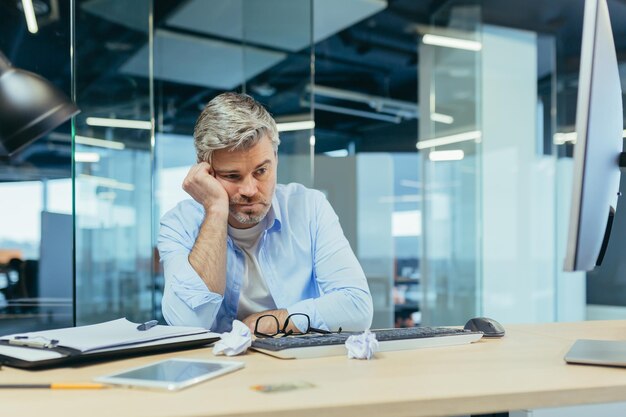 Trieste grijsharige architect man aan het werk in een modern kantoor bij een computerzakenman die aan mislukkingen denkt