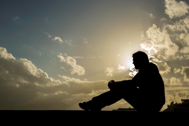 Trieste jonge man silhouet bezorgd op de steen bij zonsondergang, silhouet concept