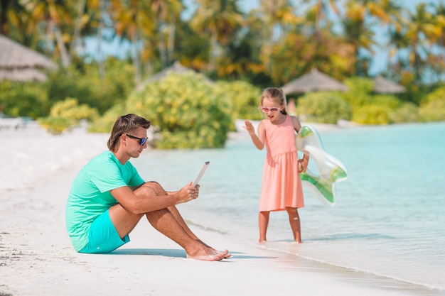 Trieste kleine kinderen wachten tot hun vader met laptop werkt om te zwemmen en plezier te hebben op het strand