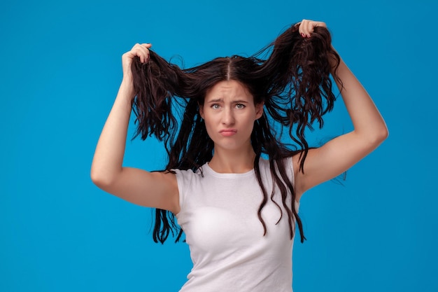 Foto trieste vrouw trekt aan haar haar op blauwe achtergrond