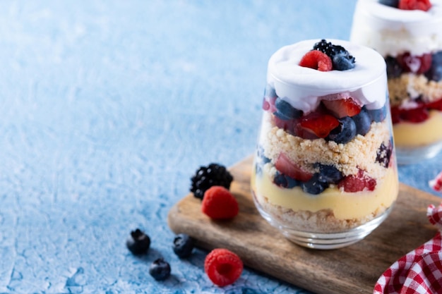 Dessert di zuppa inglese con frutti di bosco e panna su sfondo blu