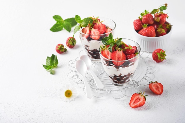 Trifles brownies fragole fresche e crema di mascarpone servite a strati su vetro su sfondo bianco dolci a porzione no cheesecake al brownie con frutti di bosco freschi in un bicchiere