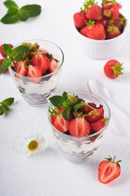 Trifles Brownies fresh strawberry and mascarpone cream servered in layers on glass on white background Portion desserts No baked brownie cheesecake with fresh berries in a glass