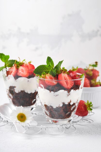 Trifles Brownies verse aardbeien en mascarpone crème geserveerd in lagen op glas op witte achtergrond Gedeelte desserts Geen gebakken brownie cheesecake met verse bessen in een glas