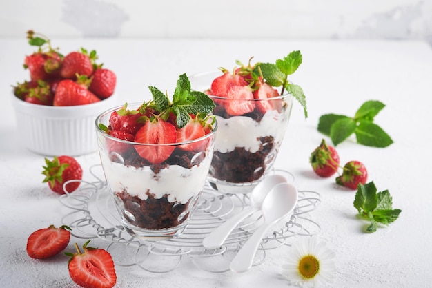 Trifles Brownies verse aardbeien en mascarpone crème geserveerd in lagen op glas op witte achtergrond Gedeelte desserts Geen gebakken brownie cheesecake met verse bessen in een glas