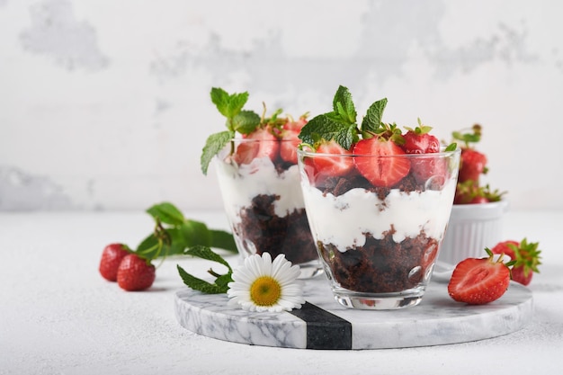 Trifles Brownies verse aardbeien en mascarpone crème geserveerd in lagen op glas op witte achtergrond Gedeelte desserts Geen gebakken brownie cheesecake met verse bessen in een glas