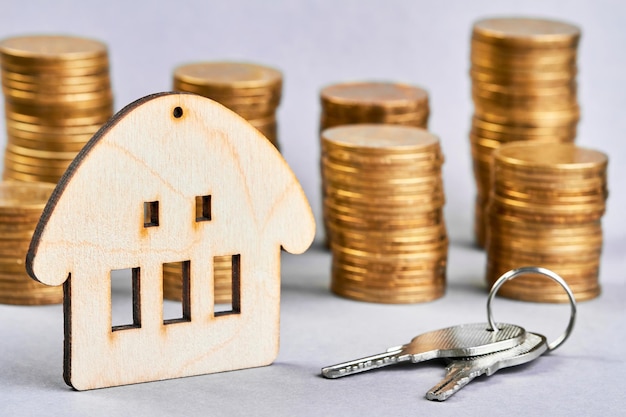 Trinket in the form of a house with the keys to the apartment on the background of stacks of coins