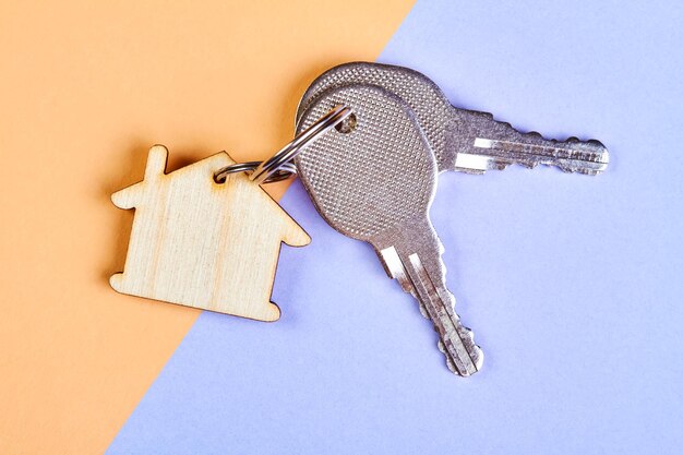 Trinket in the form of a wooden house with the keys to the apartment on the orangepurple background