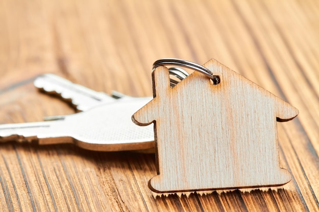 Trinket in de vorm van een houten huis met de sleutels van het appartement op houten achtergrond