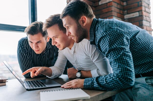 A trio of young professionals in an office astonished and dumbfounded by the work on their laptop screens they continue to work tirelessly amazed at what they've uncovered