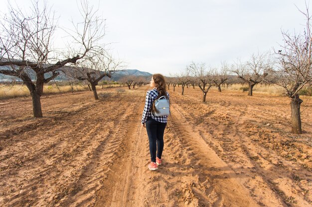 Trip, fashion and people concept - happy young woman walking with small bag and smiling over the nature.