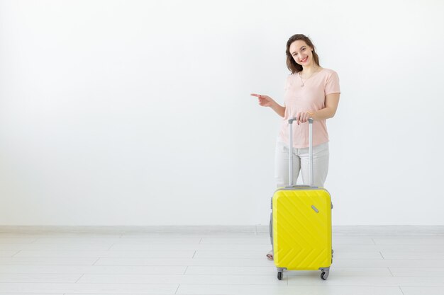 Trip, travel and holidays concept - woman with her yellow suitcase point on copy space