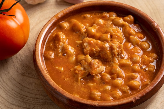 Tripe with chickpeas in clay pot on wooden table