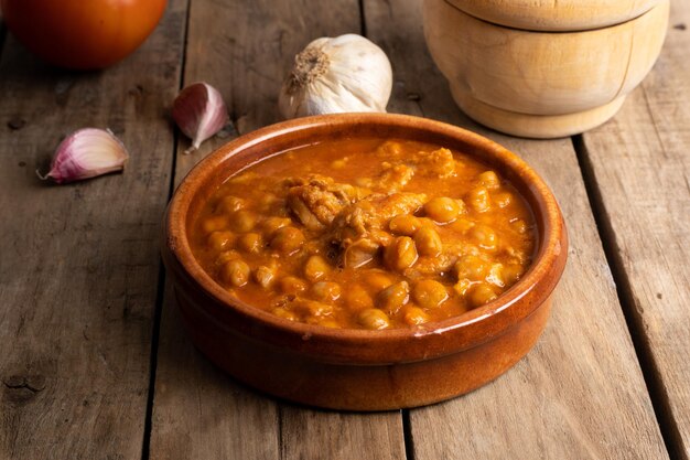 Tripe with chickpeas in clay pot on wooden table