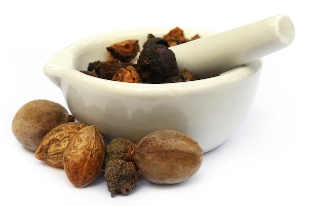 Triphala, a combination of ayurvedic fruits with mortar and pestle over white background