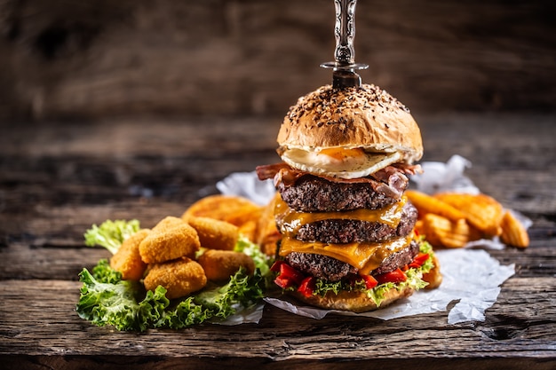 Triple beef burger met een eitje en kaasnuggets ernaast in een donkere houten omgeving.