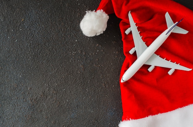 Trips or Christmas travel planning. Toy airplane and Santa hat on dark concrete.