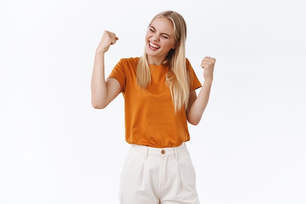 Triumphing good-looking blond modern stylish girl accomplish her goal, enjoying taste of success, fist pump say yeah, do champion dance, celebrate victory, standing white background delighted