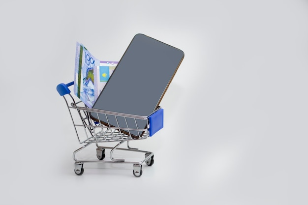 In the trolley on a white background is a phone with a tenge bill buying a phone or paying through