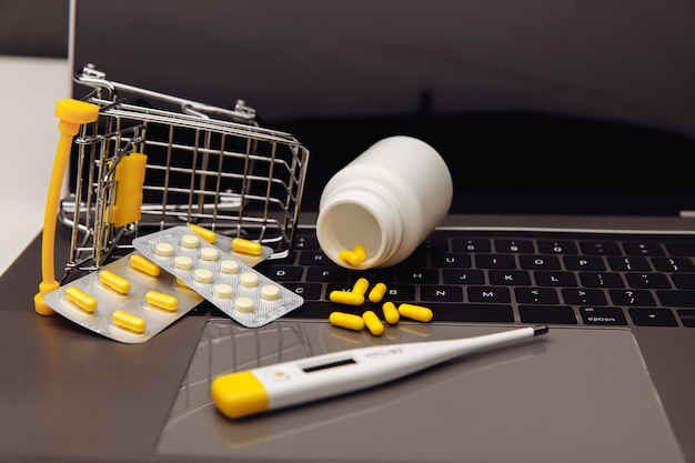 Тележка с таблетками на клавиатуре ноутбука и медицинскими инструментами. Интернет-магазины с доставкой на дом.