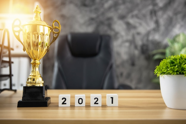 Trophy award of winner with cute year number 2021 on working wood table in office, success and win concept