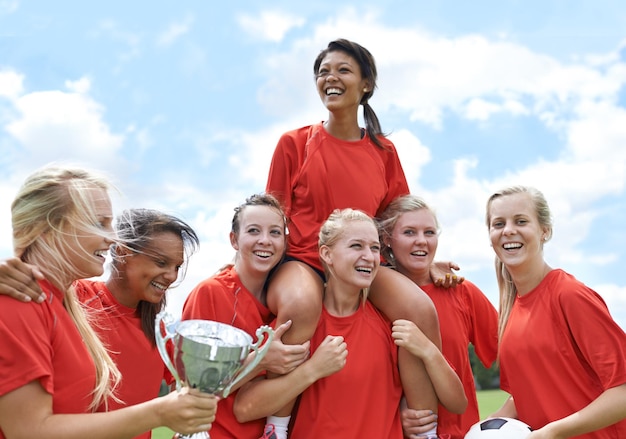 写真 勝利の達成とフィールドでの試合の成功を祝うトロフィーの勝者と女子サッカーチーム フットボール賞とお祝いの競争や目標のチャンピオンを持ち上げる女性の10代のスポーツグループ