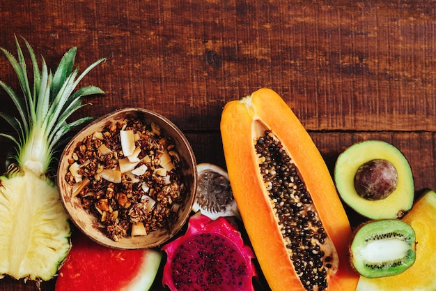 Tropic fresh summer fruits and granola seeds on brown wooden background