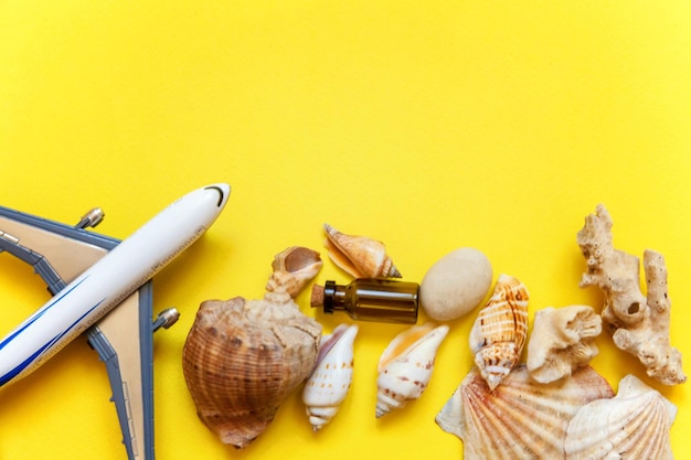 Tropical Background Seashell miniature toy plane and glass bottle on yellow colourful trendy modern fashion background Vacation travel summer weekend sea adventure trip concept