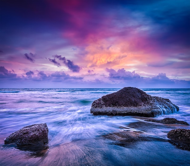 Tropical beach vacation background waves and rocks on beach on sunset with beautiful cloudscape