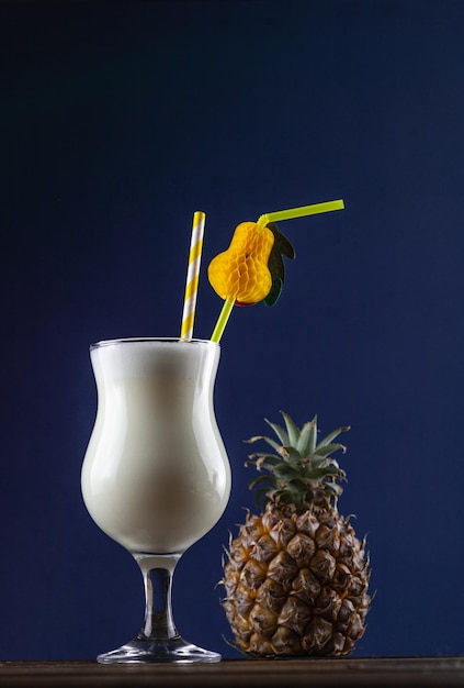 A tropical cocktail in a glass next to a pineapple. Pina colada cocktail in a glass with a straw