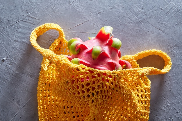 Tropical Dragon fruit in a string bag on a gray concrete surface. Shopping food with eco friendly bag.