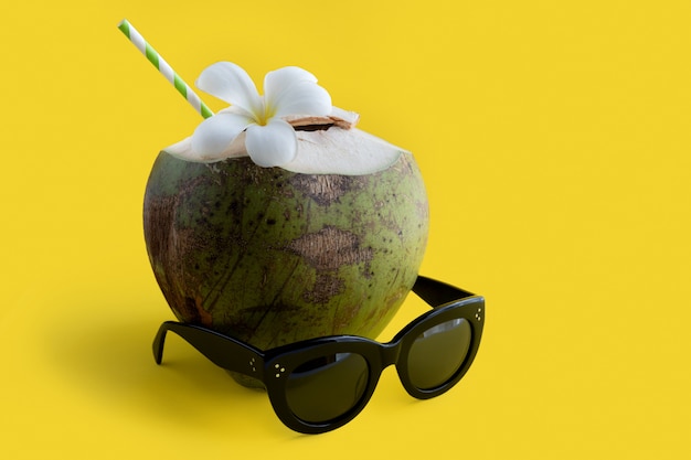 写真 黄色の背景にサングラスをかけた熱帯の新鮮なココナッツカクテルの装飾が施されたプルメリア。