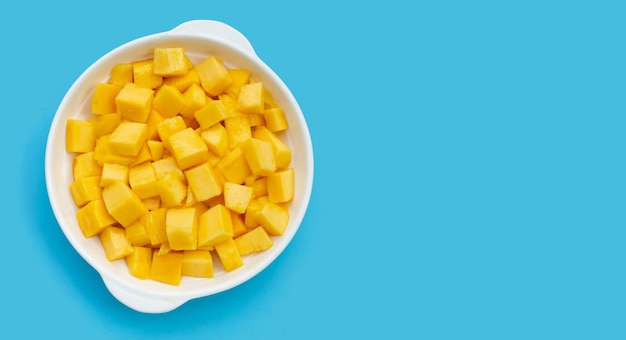 Frutta tropicale, fette di cubo di mango in una ciotola bianca su sfondo blu.