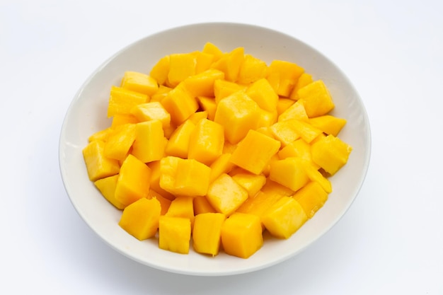 Тропические фрукты, кусочки кубика манго в белой тарелке на белом фоне.